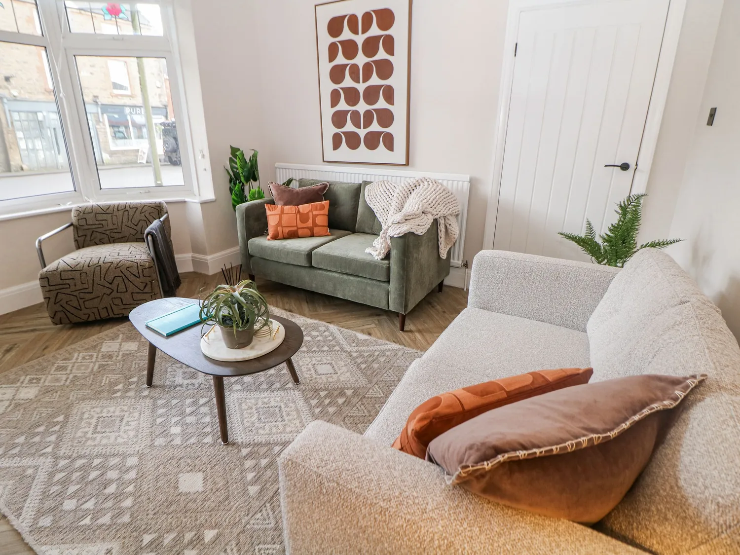 Sitting room with green velvet and grey boucle sofas beneath a bay window