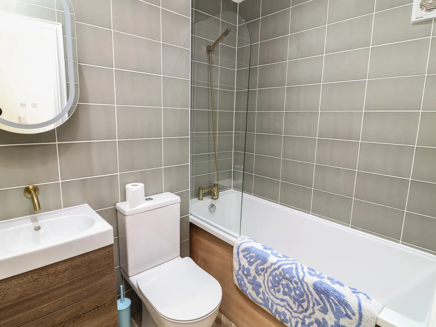 Grey-tiled bathroom with bath, shower screen and brass fixtures