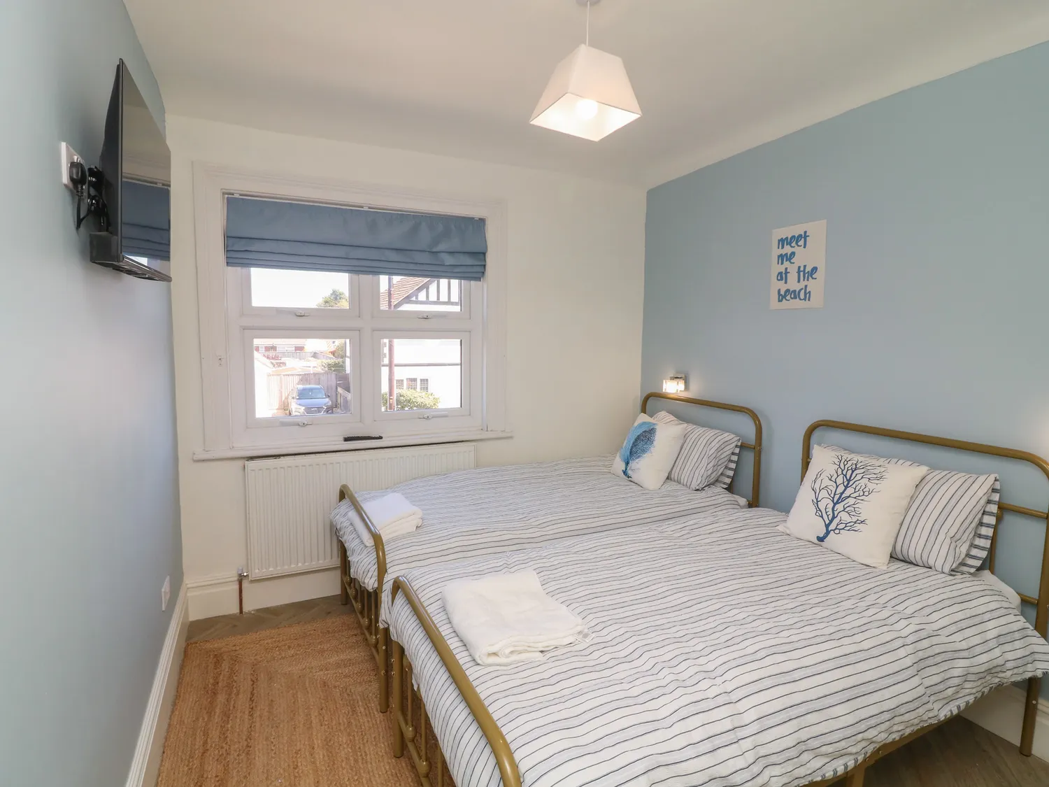 Twin bedroom with gold-frame beds and 'meet me at the beach' sign