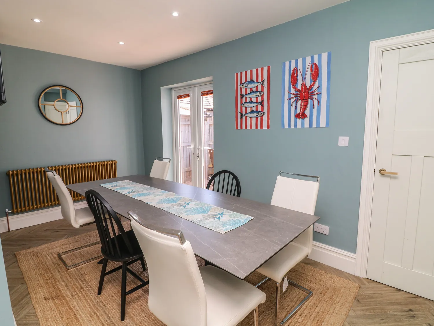 Dining room with grey table, lobster and fish prints and brass radiator