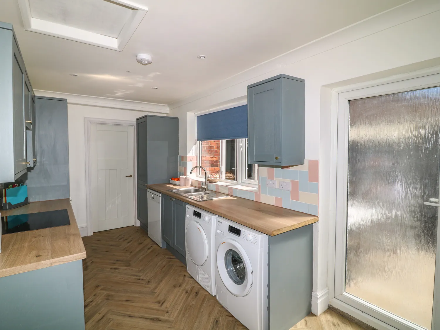 Blue-grey shaker kitchen with washer, dryer and pastel splashback